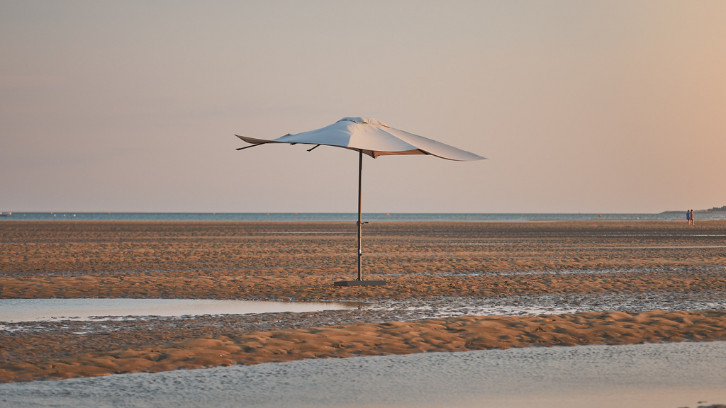 Una sombrilla recta con tela color crema sobre la arena